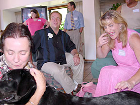 Bev and Marikay with big smiles meeting black lab. Justin watching in the background.